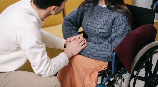 Grafika tematyczna - opiekun w raz z zosobą z niepełnosprawnością siedzącą na wózku inwalidzkim